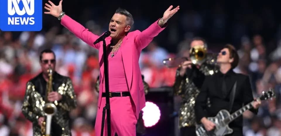 Robbie Williams performing in pink outfit with band
