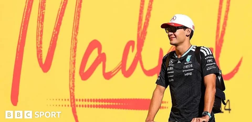 Pilote de Formule 1 sur un vélo devant une affiche
