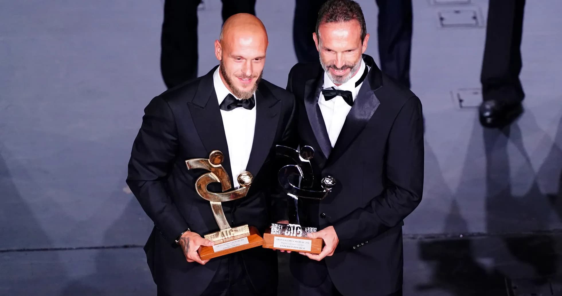 Deux hommes en costume tenant des trophées lors d'une cérémonie Deux hommes en costume tenant des trophées lors d'une cérémonie