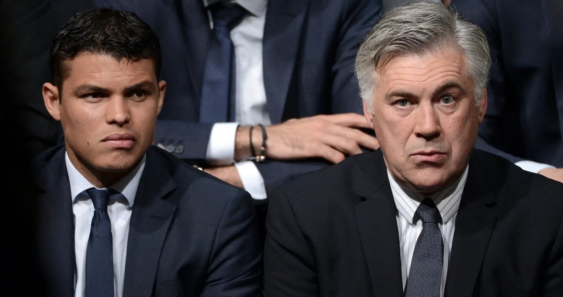 Deux hommes en costume assis, attentifs lors d'un événement Deux hommes en costume assis, attentifs lors d'un événement